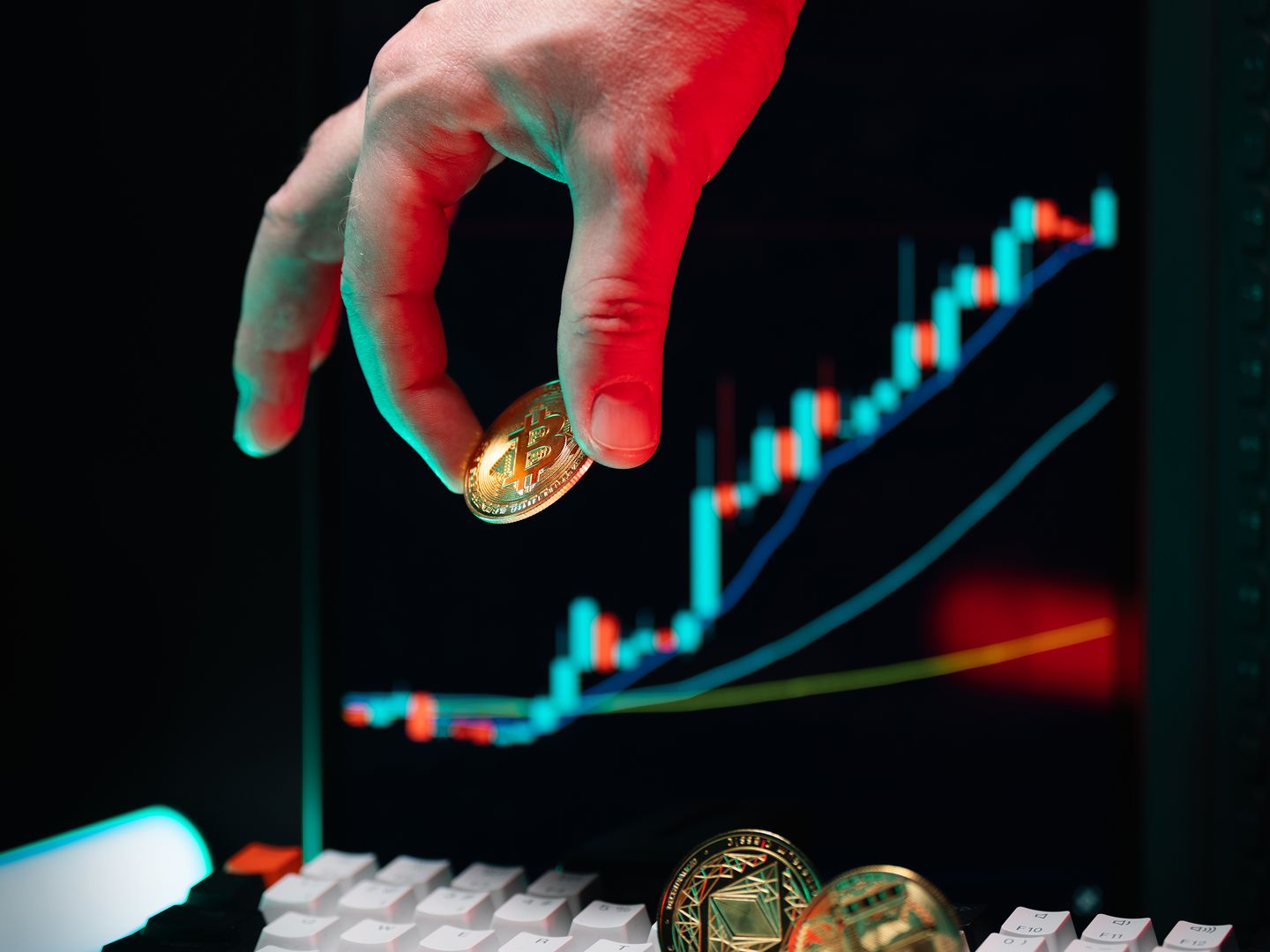 Hand holding Bitcoin with an upward cryptocurrency market chart on screen displaying growth.