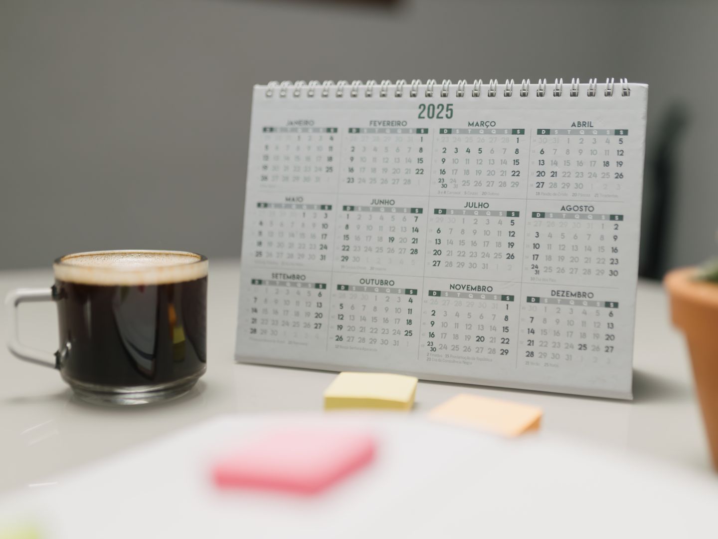 A 2025 calendar on a desk with coffee, sticky notes, and a plant in an office setting.