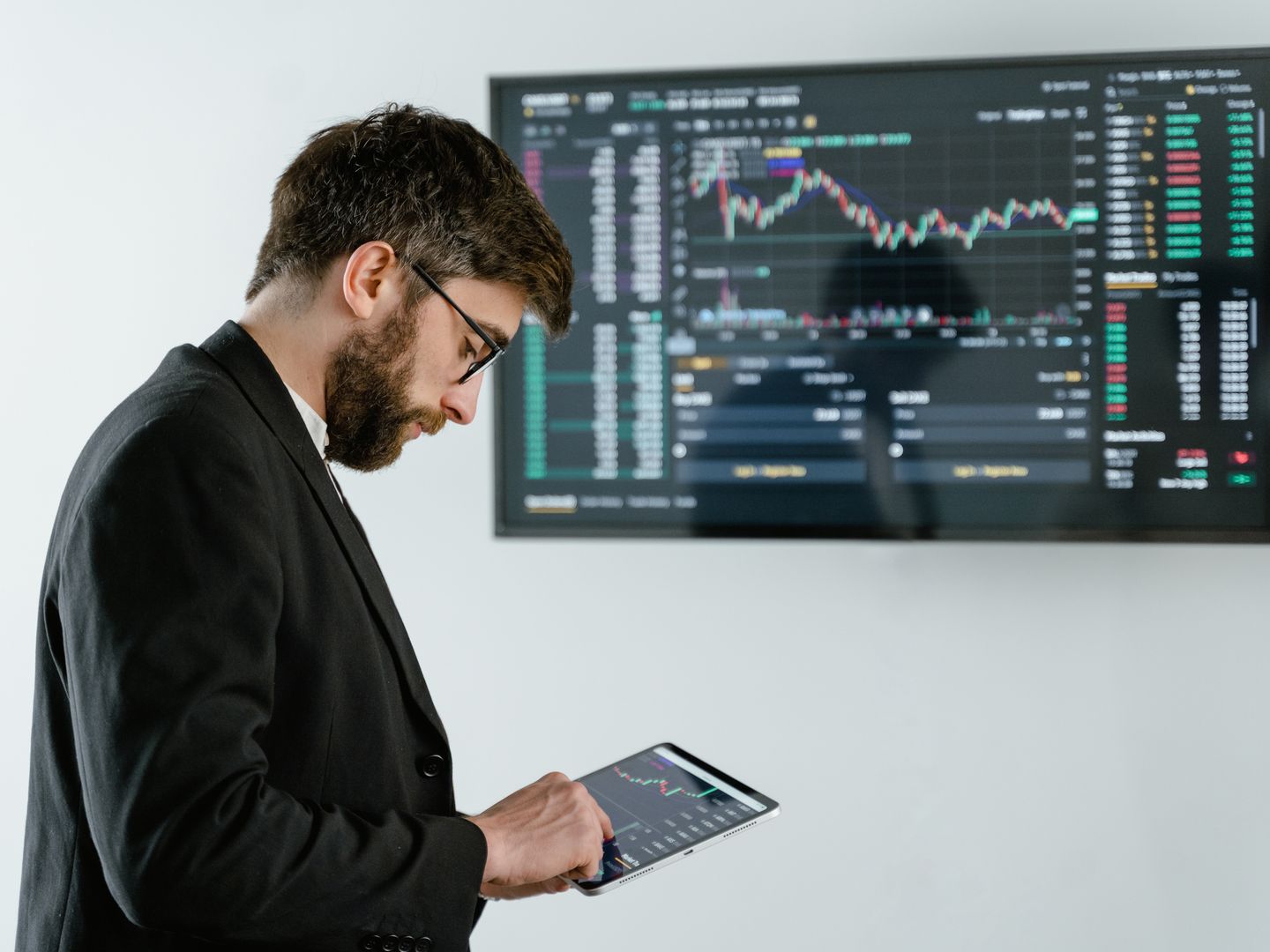 Professional man using tablet in front of cryptocurrency trading screen indoors.